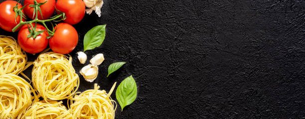 istock Raw tagliatelle pasta and tomatoes on black background 1338752686