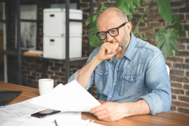 mature adult man working from office ( with laptop, paperwork, negative emotion) - arquivando documentos imagens e fotografias de stock