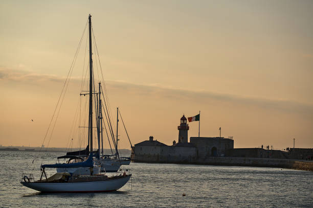 Sailboats mooring near red East Pier lighthouse with Irish flag in Dun Laoghaire harbor stock photo
