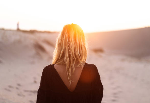 vue arrière d’une belle femme blonde au coucher ou au lever du soleil - beach sunset sea sunrise photos et images de collection