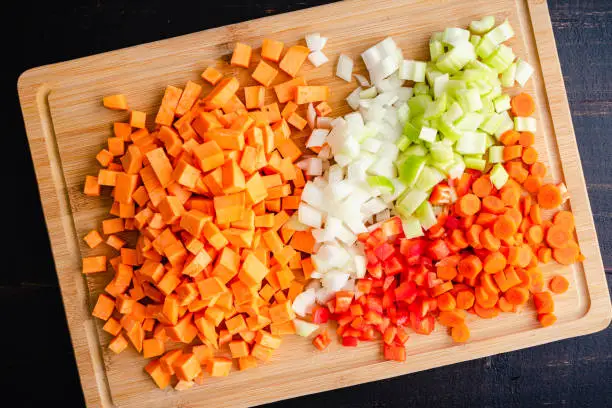 Peeled and diced sweet potatoes, onion, celery, carrots, and red bell pepper on a wood cutting board
