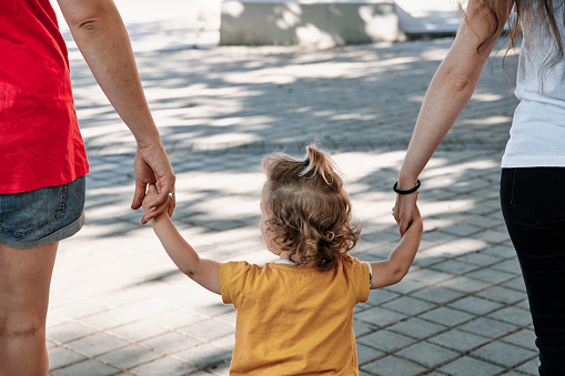 close-up of a lesbian couple walking hand in hand with their daughter through the city.