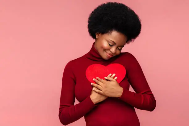 Photo of Happy african woman embracing red heart shaped postcard from lover or boyfriend on valentines day