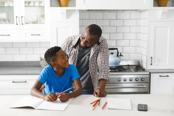 istock Smiling african american father and his son in kitchen, doing homework together 1338772112