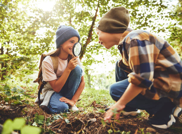istock Smiling girl looking through magnifying glass at boy while squat 1338773608