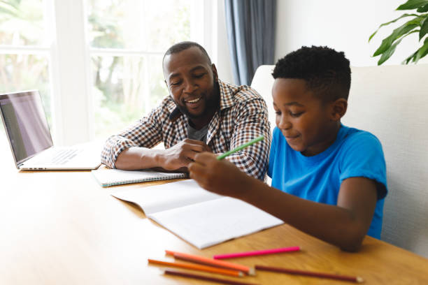 istock Smiling african american father and son sitting at table in dining room, working and doing homework 1338774469