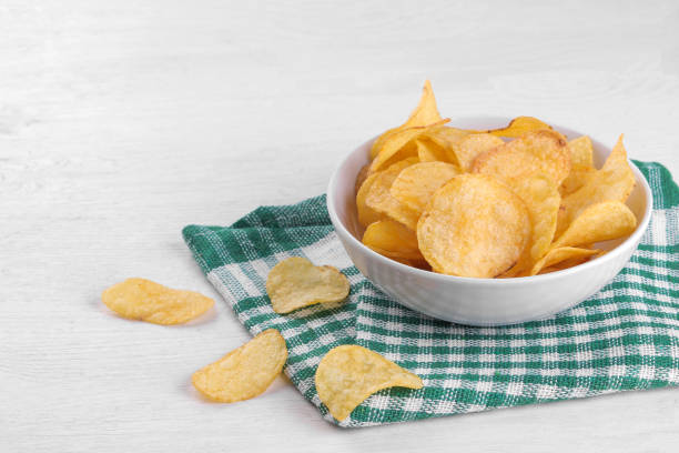 chips dans un bol blanc sur une serviette verte sur une table en bois blanc - acute pain photos et images de collection