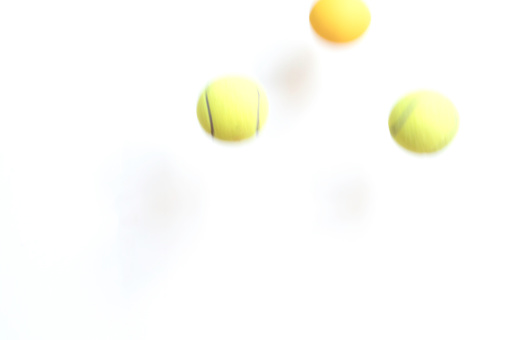 Three bouncing yellow balls in blurred motion. Two are tennis balls and one is a bouncy rubber ball. The shadows of the balls can be seen on the neutral background.