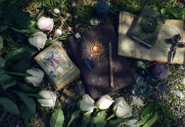 Wicca ritual with beautiful roses, tarot cards, grimoire book and magic objects.  Esoteric, gothic and occult background, Halloween mystic and wicca concept outdoors.