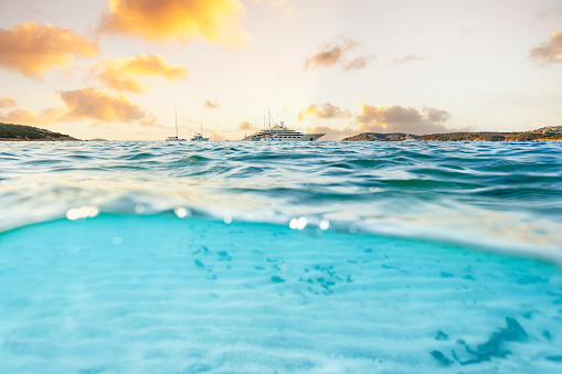 (Selective focus) Split shot, over under picture. Half underwater half sky with a luxury yacht sailing on a turquoise water during a stunning sunrise. Grande Pevero Beach, Sardinia, Italy.