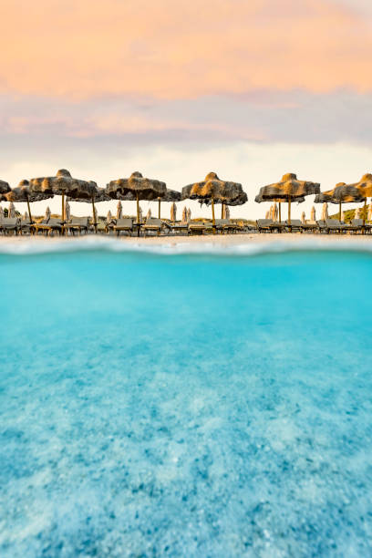 istock (Selective focus) Split shot, over under picture. Crystal clear, turquoise water and some beach umbrellas illuminated during a stunning sunrise. Grande Pevero Beach, Sardinia, Italy. 1338793315