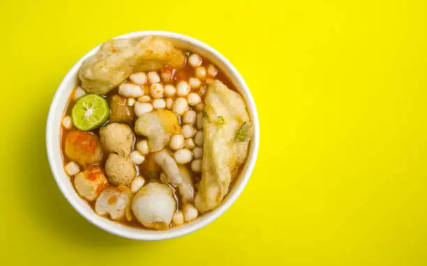 Photo of Seblak, Indonesian spicy and sour savory food on white bowl with yellow background, high angle