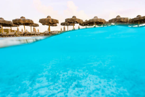 istock (Selective focus) Split shot, over under picture. Crystal clear, turquoise water and some beach umbrellas illuminated during a stunning sunrise. Grande Pevero Beach, Sardinia, Italy. 1338793885