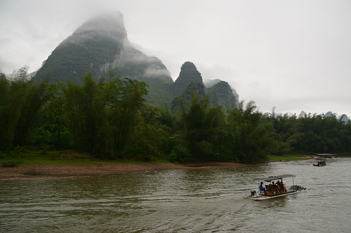 Tourists on wooden raft sightseeing the Karst mountains in the fog on Lijiang river, Guangxi province, China.