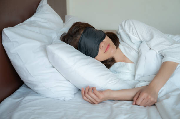 Portrait of young beautiful woman wearing sleep mask during sleeping on the bed. A sleep mask can block out light when sleeping, allows the user to achieve a deeper level of sleep. sleep eye mask stock pictures, royalty-free photos & images