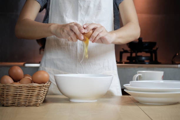 흰 앞치마를 입은 여성 요리사가 집 부엌에서 달걀을 부수고 있습니다. - eggs bowl cracked dining table 뉴스 사진 이미지