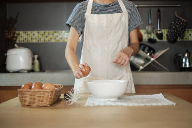 흰 앞치마를 입은 여성 요리사가 집 부엌에서 달걀을 부수고 있습니다. - eggs bowl cracked dining table 뉴스 사진 이미지