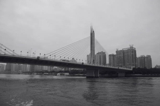 Anhui Hongcun, China – January 01, 2018: A black and white view of a traditional Chinese village with stone bridge and reflective water under a cloudy sky. People standing in distance