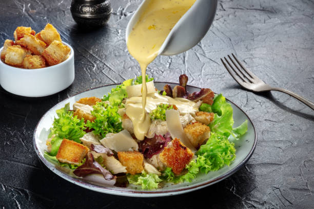 Chicken Caesar salad with the classic dressing being poured and croutons Chicken Caesar salad with the classic dressing being poured, croutons, and pepper, on a black background salad dressing photos stock pictures, royalty-free photos & images