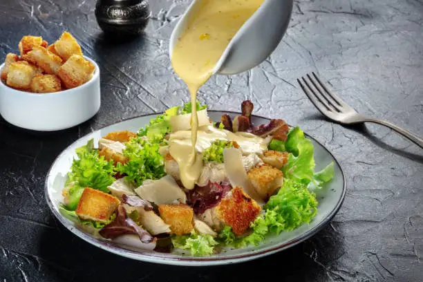 Photo of Chicken Caesar salad with the classic dressing being poured and croutons