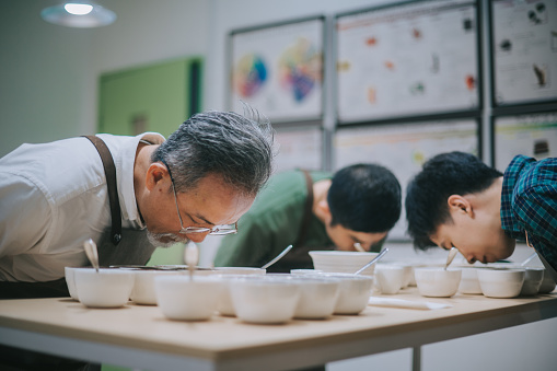 professional Asian Chinese barista grader performing coffee cupping bending over smelling coffee closely
