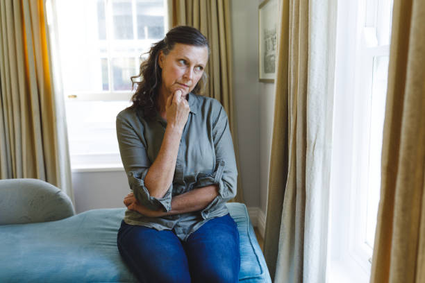 istock Thoughtful senior caucasian woman sitting on sofa and looking through window 1338803549