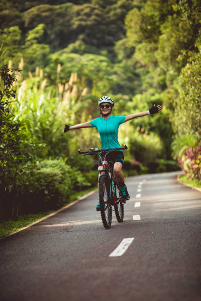 woman no handed cycling on tropical park trail in summer - beautiful blue sport vertical imagens e fotografias de stock