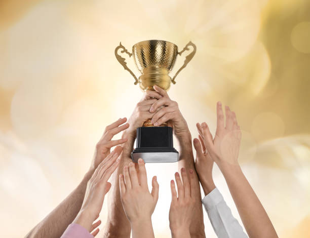 istock People with gold trophy cup on color background, closeup 1338810187