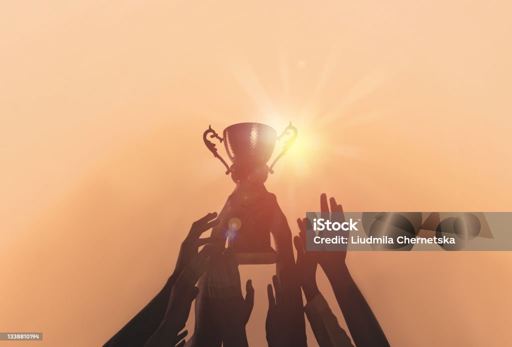 People with gold trophy cup on color background, closeup Winning Stock Photo