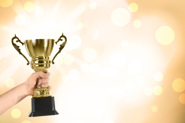 istock Man holding gold trophy cup on color background, closeup. Space for text 1338810214
