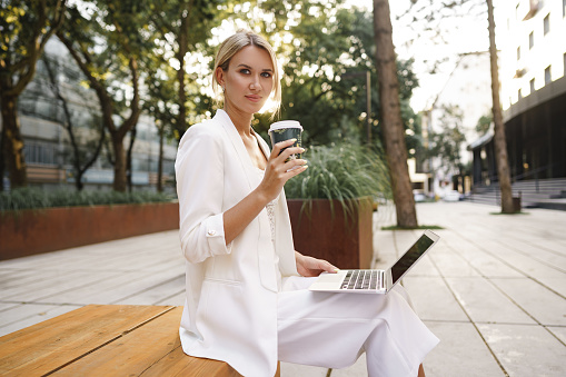 Young beautiful businesswoman working on laptop, sitting on the bench in the street, close up