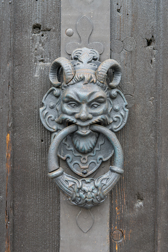 scary door knocker as a devil on an old wooden door in Austria