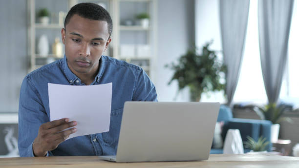 istock Young African Man Working on Documents and Laptop in Office 1338814601