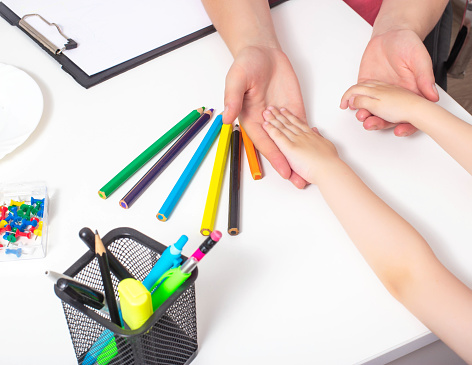 Hands of an adult and a child on the table with multi-colored pencils. The concept of psychological assistance to children, the development of stress resistance, medical center