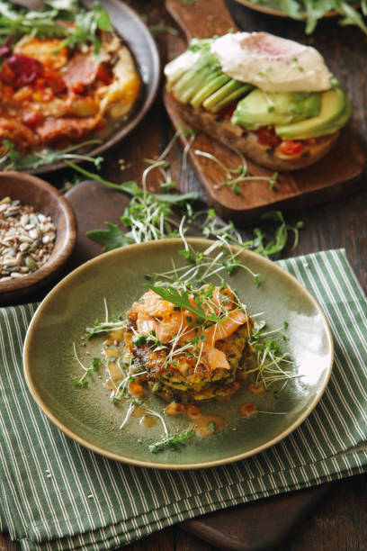 Healthy breakfast Zucchini fritters with cold-smoked salmon and avocado bruschetta with baked vegetables and cream cheese. Fried eggs. Close-up composition on wooden background food styling stock pictures, royalty-free photos & images