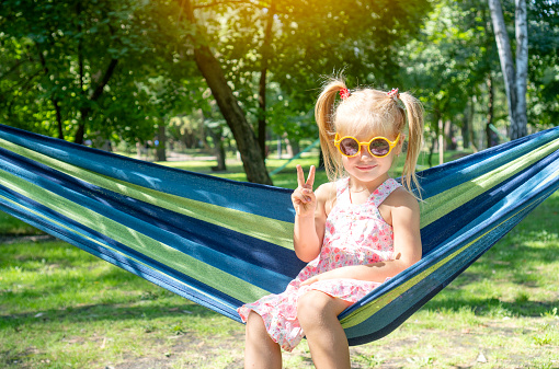 Cute little girl showing with fingers the symbol of victory, while resting on a hammock in the park