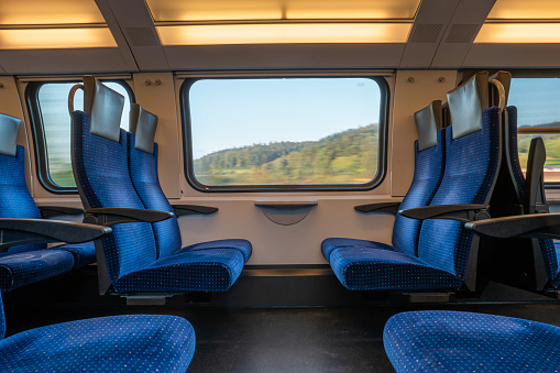 Blue empty opposing seats in a moving train. Large window with blurred landscape, daytime, summer, no people..