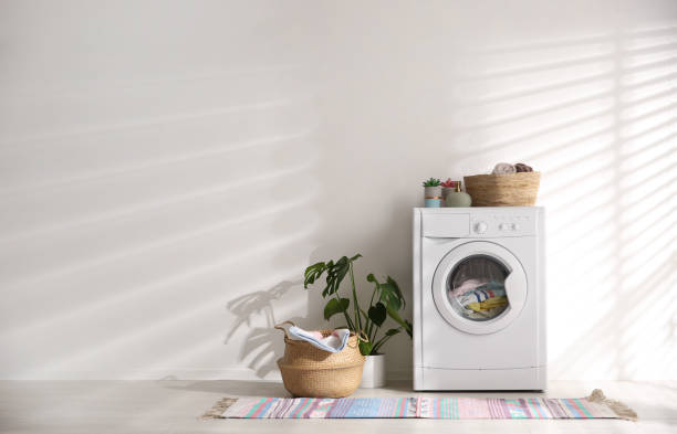 istock Modern washing machine and wicker basket with laundry near white wall, space for text. Interior design 1338831255