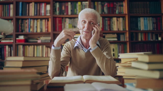 Mature male scientist giving advice over phone referring to information in books