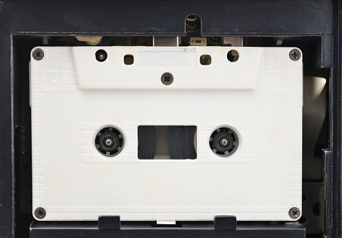 Audio cassette tape in use sound recording in the tape recorder. Vintage music cassette with a blank white label, playing back in the player.