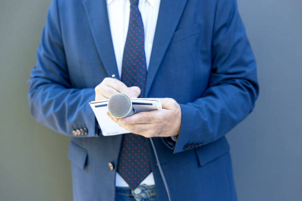 istock Well-dressed journalist at news conference or media event, holding microphone, writing notes 1338840929