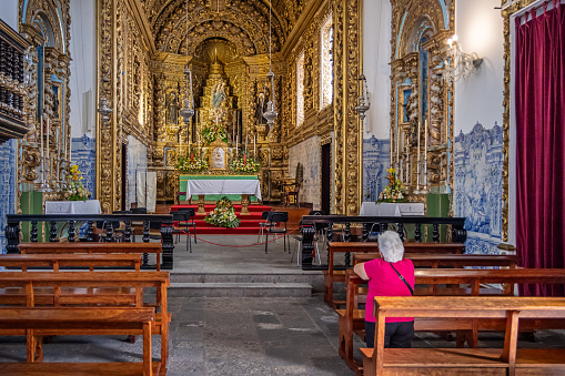 Elderly woman in front of the altar in Santuário do Senhor Santo Cristo dos Milagres - Convent of Our Lady of Hope in Ponta Delgada on the Azorean Island San Miguel. The church is from 1771 and the style has been described as baroque-to-rococo.