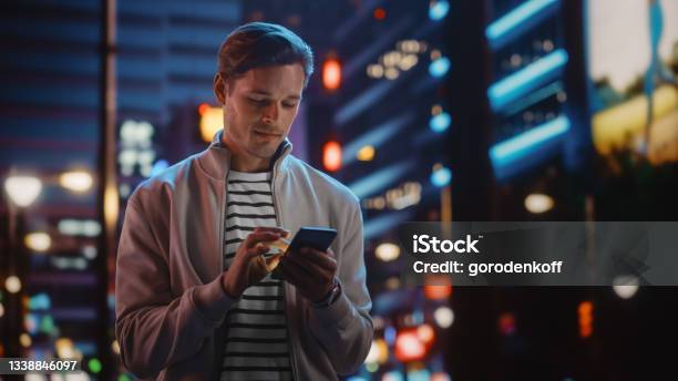 Handsome Man Using Smartphone Walking Through Night City Full Of Neon Colors And Entertainment Stylish Young Man Using Mobile Phone Posting On Social Media Online Shopping Texting On Dating App Stock Photo - Download Image Now