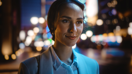 Beautiful Young Woman Walking Through Night City Street Full of Neon Lights and Entertainment Venues. Smiling Attractive Thoughtful Independent Woman Traveling. Close-up Portrait