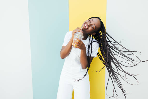 istock Cheerful woman with closed eyes drinking orange juice while dancing at a wall with blue and yellow stripes 1338846955