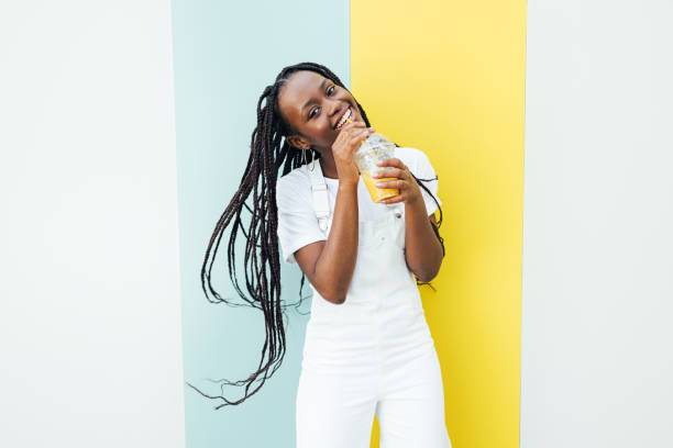 istock Playful woman in white overall drinking juice and looking at camera while standing at wall outdoors 1338847023