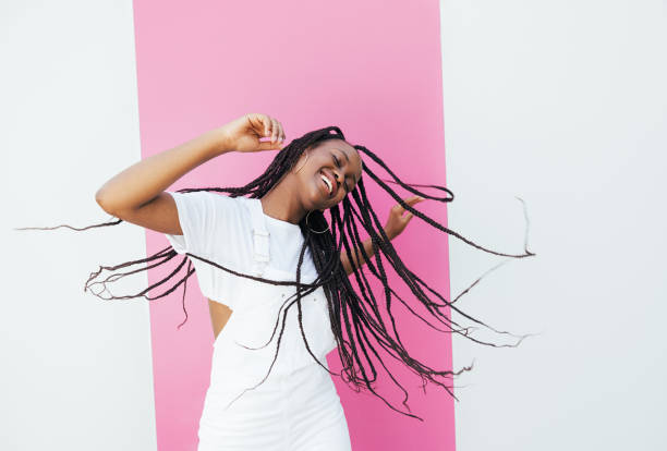 playful woman with long braided hair dancing at a white wall with pink stripe - braided braids women long hair imagens e fotografias de stock