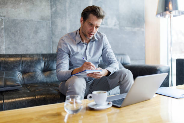 istock Businessman taking notes while working on laptop in a lobby. 1338847667