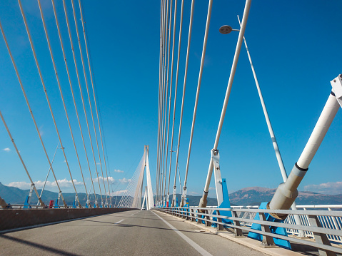Driving Rion-Antirion Bridge on highway road in Patras city, Greece. Suspension bridge on Corinth Gulf. Second longest cable-stayed bridge. Sunny summer day with scenic blue sky