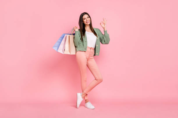 幸せなブルネットの若い女性のフル長の写真は、ピンクの色の背景に隔離された大丈夫サイン笑顔ホールドバッグを示しています - women shopping ストックフォトと画像